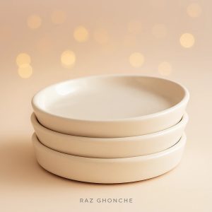 Stack of three round cream ceramic plant saucers with a smooth matte finish, placed on a beige background with warm bokeh lights.