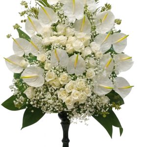 Luxury white sympathy flower arrangement with white anthuriums, white roses and gypsophila on a black stand.
