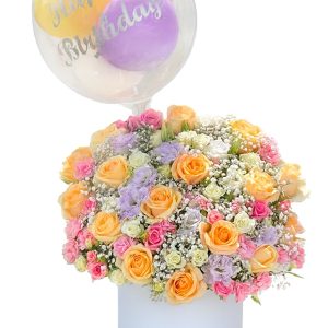 Luxury birthday flower box with peach and pink roses, pastel lisianthus, gypsophila and a clear “Happy Birthday” balloon.