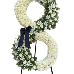 Luxury double-ring white floral stand with lilies, roses, greenery and black ribbon on a tripod.