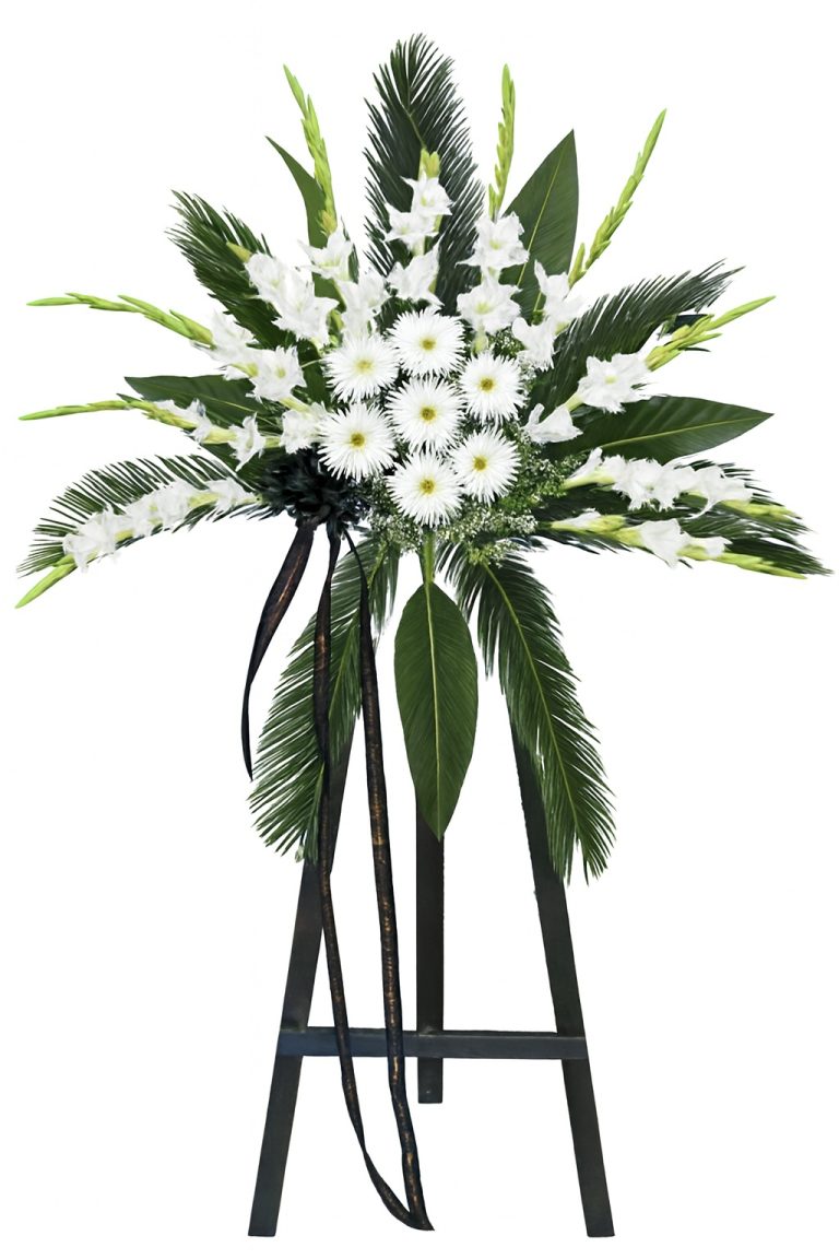 Luxury white ceremonial standing arrangement with white gladiolus, white daisies, palm leaves and black ribbon on a tall black stand.