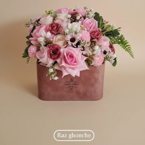 Luxurious artificial flower arrangement in a rectangular mauve velvet box, featuring a mix of pink, cream, and deep magenta silk roses and various filler flowers and greenery.