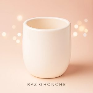 Minimalist cream-colored ceramic pot with smooth surface and rounded edges, placed on a soft peach background with warm bokeh lights.